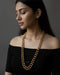 Woman wearing a long gold dholki necklace against a dark background