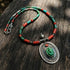 Necklace with green turquoise and red coral beads and a silver pendant on a wooden surface