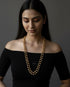 Woman wearing a long gold pure silver dholki necklace against a dark background
