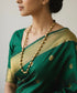 Woman wearing a green saree with gold border and dholki mala