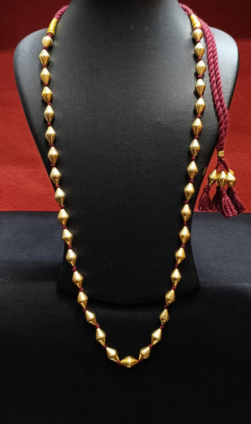 Gold dholki beaded necklace with red tassels on a black mannequin