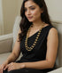Woman wearing a black dress and gold plated 925 pure silver dholki necklace sitting on a couch.