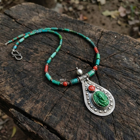 Necklace with green turquoise and red coral beads and a silver pendant on a wooden surface