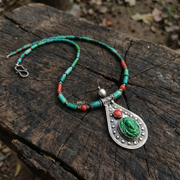 Necklace with green turquoise and red coral beads and a silver pendant on a wooden surface